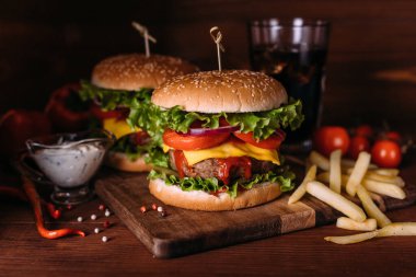 İki ev yapımı taze hamburgerle marul ve peynir ahşap kırsal masada. Patates kızartması, domates ve sos. Koyu gıda geçmişi.