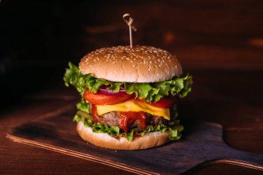 Ahşap kırsal masada marul ve peynirli ev yapımı lezzetli hamburger. Patates kızartması, domates ve sos. Koyu gıda geçmişi.