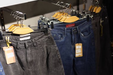 Bir mağazadaki ahşap askılarda asılı mavi ve siyah kotlar..