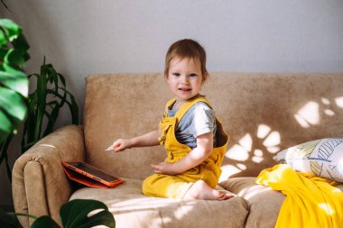 Teknolojiyi kullanan çocuk. Evde küçük bir çocuk kanepede elinde tablet ve kalem stiliyle resim çiziyor..