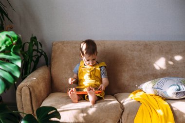 Teknolojiyi kullanan çocuk. Evde küçük bir çocuk kanepede elinde tablet ve kalem stiliyle resim çiziyor..