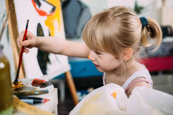 Küçük tatlı bir kız, evde akrilikle resim çiziyor.. — Stok fotoğraf