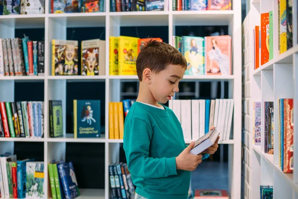 A little boy reaches for shelf of childrens books in the bookstore. — Stock Photo, Image