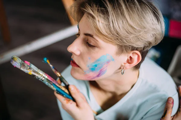 Retrato creativo de una hermosa joven artista en estudio con pinceles. —  Fotos de Stock