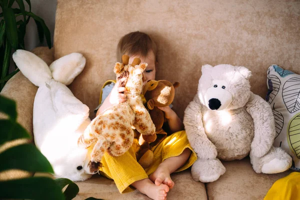 Весела маленька дитина розважається, граючи з м'якими іграшками на дивані вдома . — стокове фото