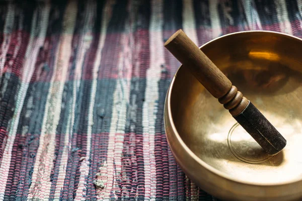 Tibetan singing bowl with a stick on a handmade woven carpet.