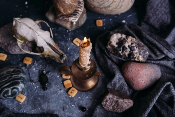 Старый череп собаки, горящая свеча, деревянные руны и камни на столе ведьмы. — стоковое фото