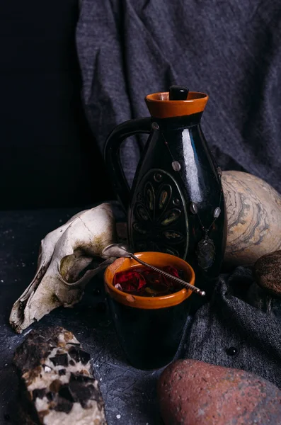 Vieux crâne de chien, cruche et pierres sur table de sorcière. Boisson enchantée aux pétales de fleurs — Photo