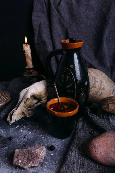 Vieux crâne de chien, cruche et pierres sur table de sorcière. Boisson enchantée aux pétales de fleurs — Photo