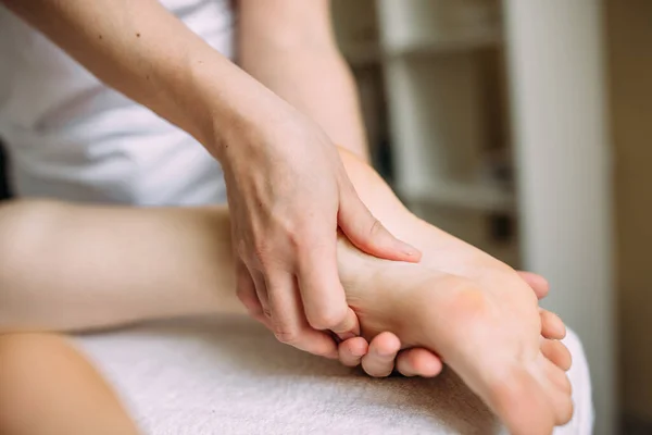 El masajista da un masaje a los pies femeninos en el spa. — Foto de Stock