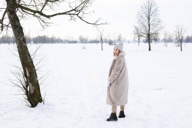 Bej elbiseli genç kız, kışın yapay kürk yürüyüşlerinden yapılmış kürk manto.