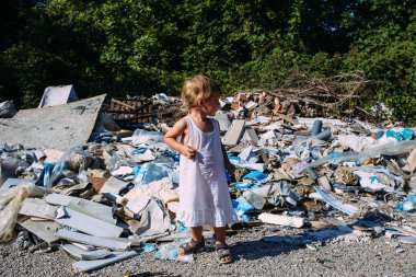 Küçük bir kız çöplükte, ormanda dağınık bir çöp yığınının arasında.. 