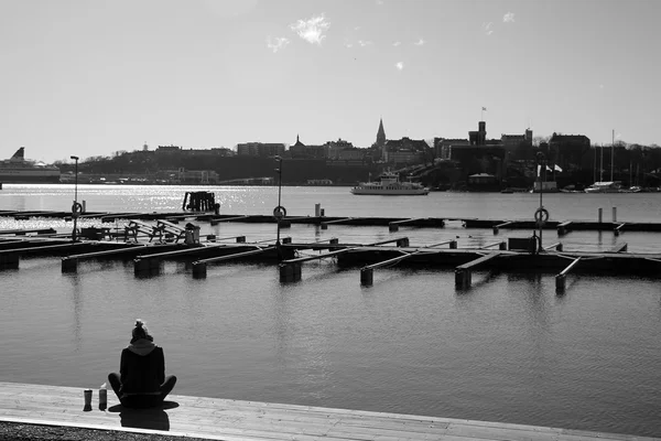 Woman sitting at the water's edge next to a dock — Zdjęcie stockowe