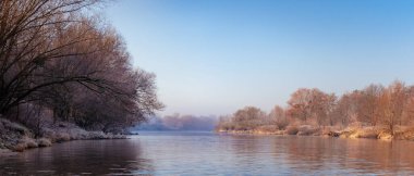 Wroclaw 'daki Odra Nehri' nde soğuk bir sabah, su yavaşça nehirden aşağı akıyor. Sahil kenarındaki sakin su ve ağaçlarla nehir yatağı, kıyıdan manzara.
