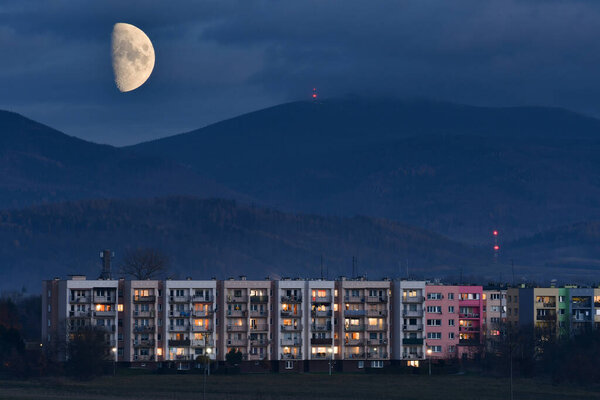 Bystrzyca Klodzka, moonrise over the city against the backdrop of mountains. The first quarter of the moon in the sky. The arriving moon is the time from new moon to full moon.