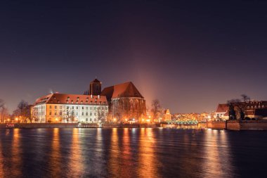Felsefe Fakültesi, Odra Nehri 'ndeki Wroclaw' daki Roma Katolik Kilisesi, gece aydınlandı. Aydınlatılmış binalar nehrin diğer tarafından görülebilir. Uzaktan Tumski Köprüsü 'nü görebilirsin..