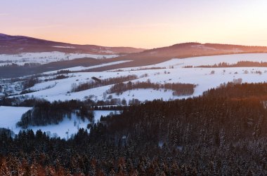 Dağ sırasının manzarası, kışın Stolowe Dağları 'nın gözcü noktasından manzarası. Gün batımında renkli gökyüzü olan kış manzarası.