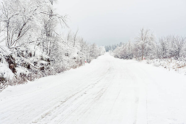 Winter landscape with snow-covered trees on the mountain road. Sudetes covered with white snow. A cloudy day with fog limits visibility in the mountains.