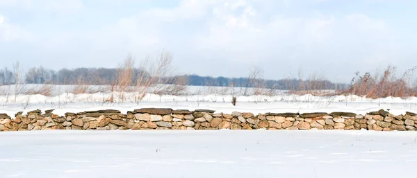 A stone fence covered with white snow on a sunny day.