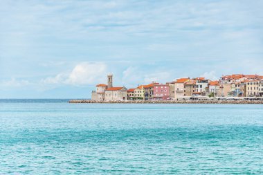 Slovenya 'nın sahil kenti Piran, deniz kenarındaki binaların manzarası ve gezinti alanının sonundaki Piranski svetilnik turizm merkezi.