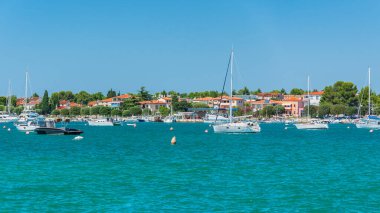 Hırvatistan 'ın Umag kasabasında güneşli bir yaz gününde gezinti güvertesinden seyredilen demirlemiş teknelerle dolu küçük bir koy..