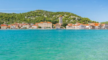 Hırvatistan 'ın Tisno kıyı kenti alçak dağlar ve mavi sularla çevrili deniz kıyısında yer alıyor. Güneşli bir günde yaz manzarasından bir manzara..