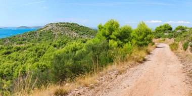 Hırvatistan 'ın yeşil tepeleri ve deniz kıyısında mavi suları olan kıyı manzarası, tepeden doğaya çakıllı bisiklet yolunun güneşli bir günde manzarası.