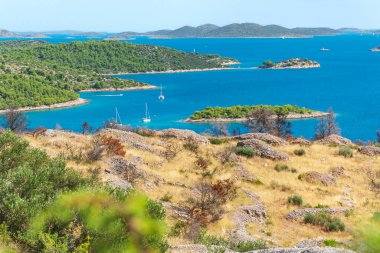 Denizde küçük adaları, yeşil ormanı ve mavi suları olan Hırvat kıyı manzarası, güneşli bir günde bir tepeden manzaralı.