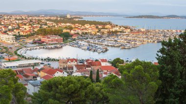 Hırvatistan 'ın Tribunj kenti deniz kenarında, marinanın akşam manzarası ve dağın tepesinden şehrin bir kısmı..
