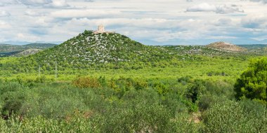 Dağın tepesinde yeşil tepeler ve Katolik kilisesi olan Hırvat manzarası, bulutlu güneşli bir günde tepedeki bisiklet yolunun manzarası.