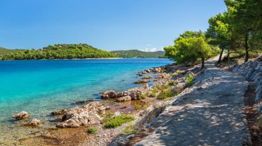 Açık mavi suları olan doğal kayalık bir sahil şeridi. Güneşli bir günde kıyı şeridinden uzak yeşil adalara bir manzara.