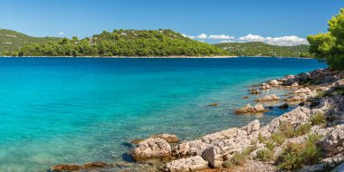Açık mavi suları olan doğal kayalık bir sahil şeridi. Güneşli bir günde kıyı şeridinden uzak yeşil adalara bir manzara.