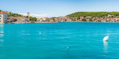 Hırvatistan 'ın sahil kenti Tisno, deniz kıyısında evleri olan tepeler, güneşli bir yaz gününde deniz kenarındaki yürüyüş yolu manzarası.