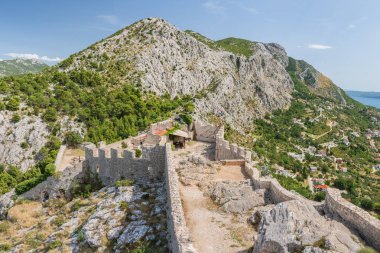 Hırvatistan 'ın sahil kenti Omis dağların eteklerinde yer alıyor ve Mirabela Kalesi ve çevresindeki dağların manzarası güneşli bir günde bir dağ manzarasına sahip..