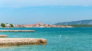Hırvatistan 'ın Tisno kıyı kenti alçak dağlar ve mavi sularla çevrili deniz kıyısında yer alıyor. Güneşli bir günde yaz manzarasından bir manzara..