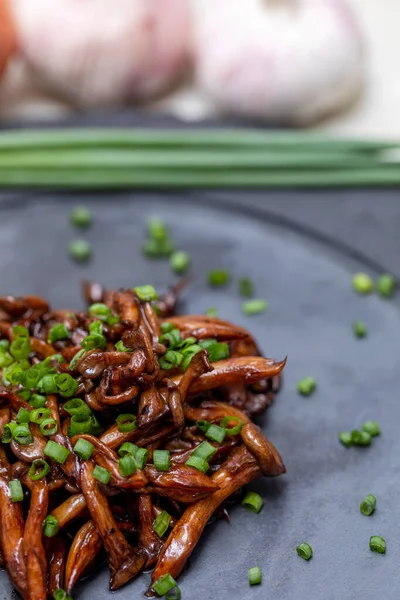 Shimeji mushroom served with chives on black stone plate. Typical oriental meal. Detail of food dish, closeup, selective focus.