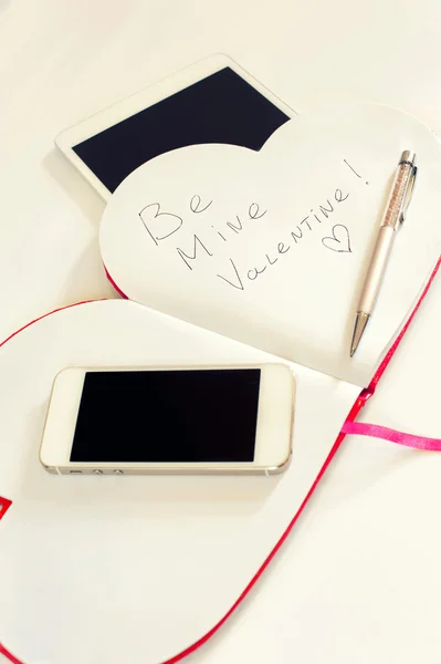 Smartphone en Valentine love bericht in hart vorm notitieblok. — Stockfoto
