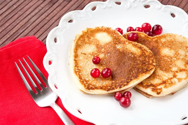 Herzförmige Pfannkuchen mit Preiselbeeren auf Porzellanteller. schließen — Stockfoto