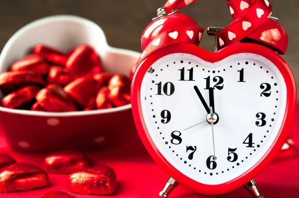 Liebe herzförmige rote Uhr und süße Pralinen. Zeit für die Liebe. — Stockfoto