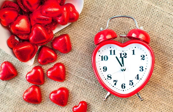 E 'ora dell'amore. Orologio a forma di cuore rosso con cioccolatini dolci . — Foto Stock