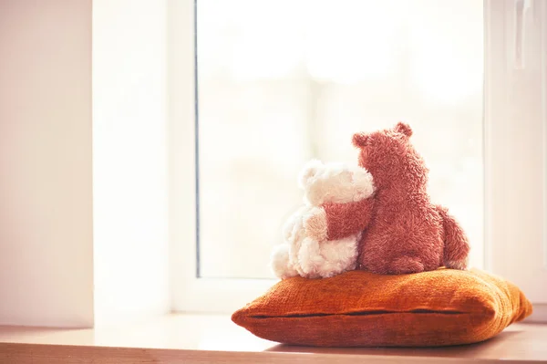 Two embracing teddy bear toys sitting on window-sill — Stock Photo, Image