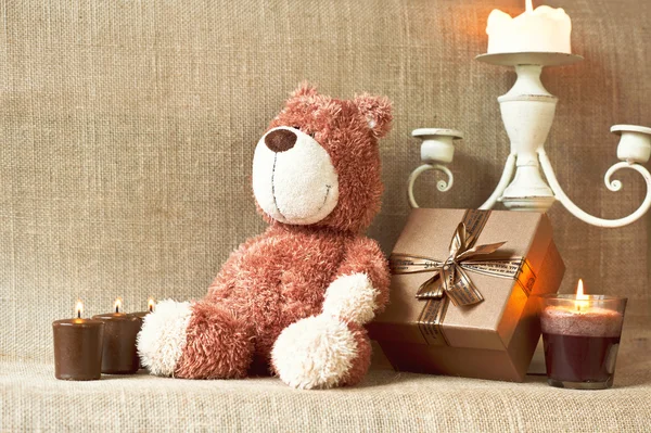 Romantic present. Teddy bear toy with gift box and candles. — Stock Photo, Image