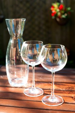 Two transparent shiny empty wineglasses and carafe in rays of su