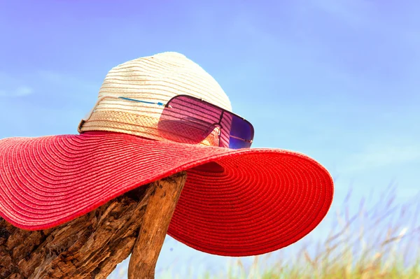 Chapeau d'été rouge élégant pour femme avec lunettes de soleil sur fond bleu ciel — Photo