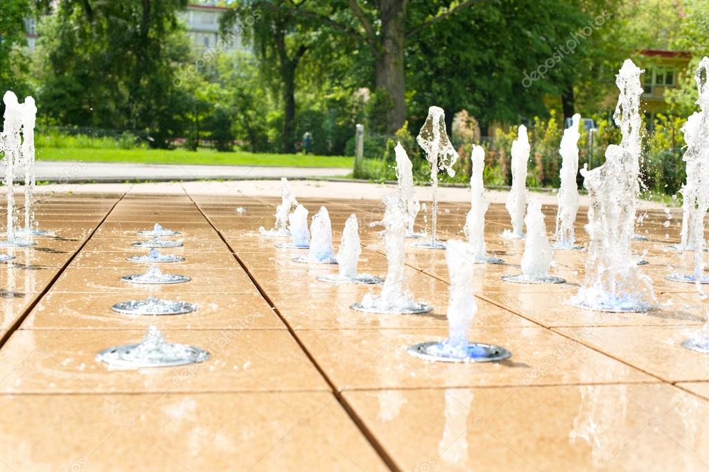 Many small splashing dancing fountains in summer Warsaw park