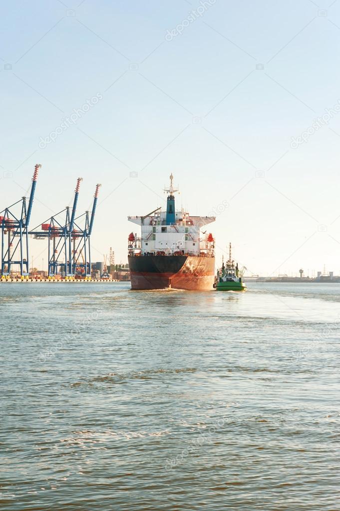 Tugboat assisting bulk cargo ship in a harbor. Front view.