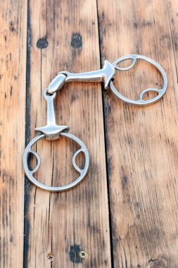 Steel horse snaffle-bit on wooden background.