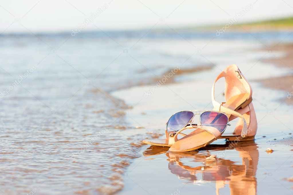 Fashionable women sandals and sunglasses on summer sandy wet coa