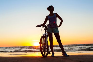 Günbatımı çok renkli arka plan üzerinde bisiklet ile sportif kadın silüeti