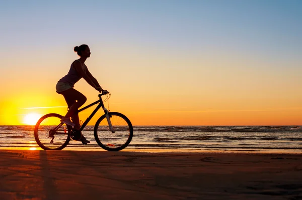 Silhouette of sporty woman riding bicycle on multicolored sunset — Stock Photo, Image